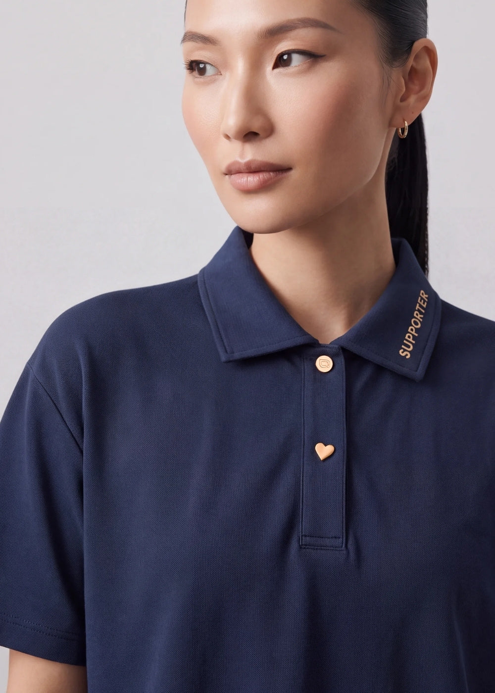 Close-up of a navy blue polo shirt featuring gold 'SUPPORTER' text on the collar and gold heart-shaped buttons.