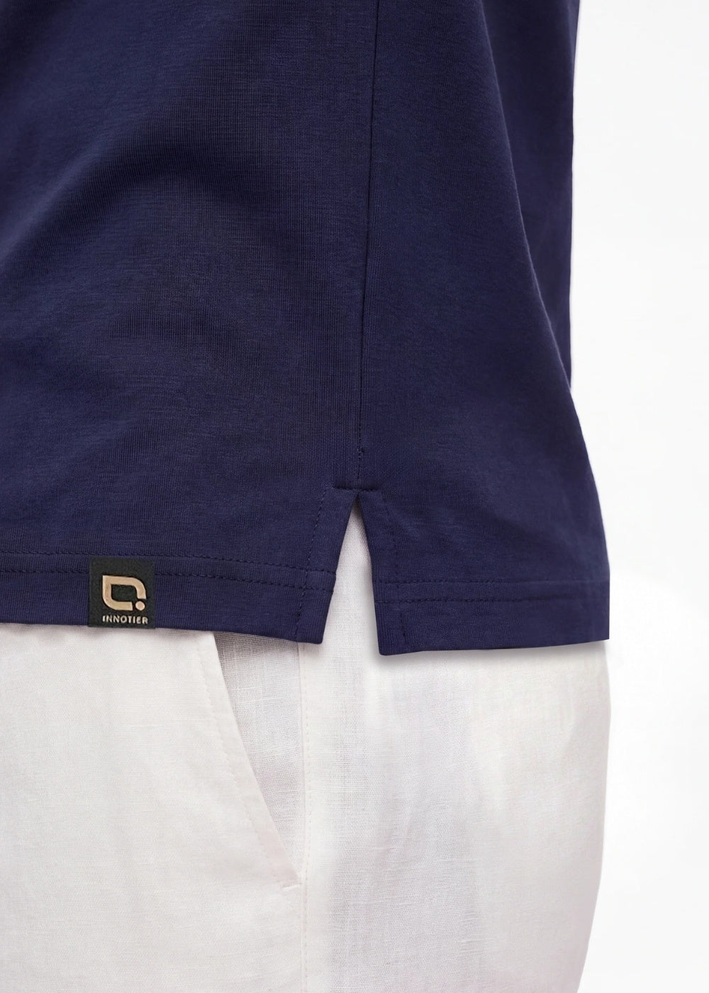 Close-up of the side hem split on a navy blue INNOTIER polo shirt with a black and gold brand tag
